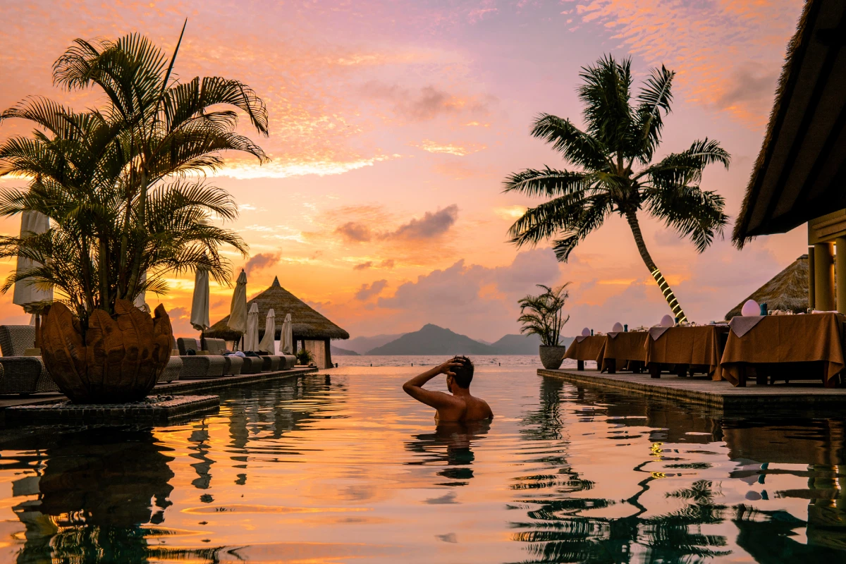 Man relaxing in infinity pool at sunset.